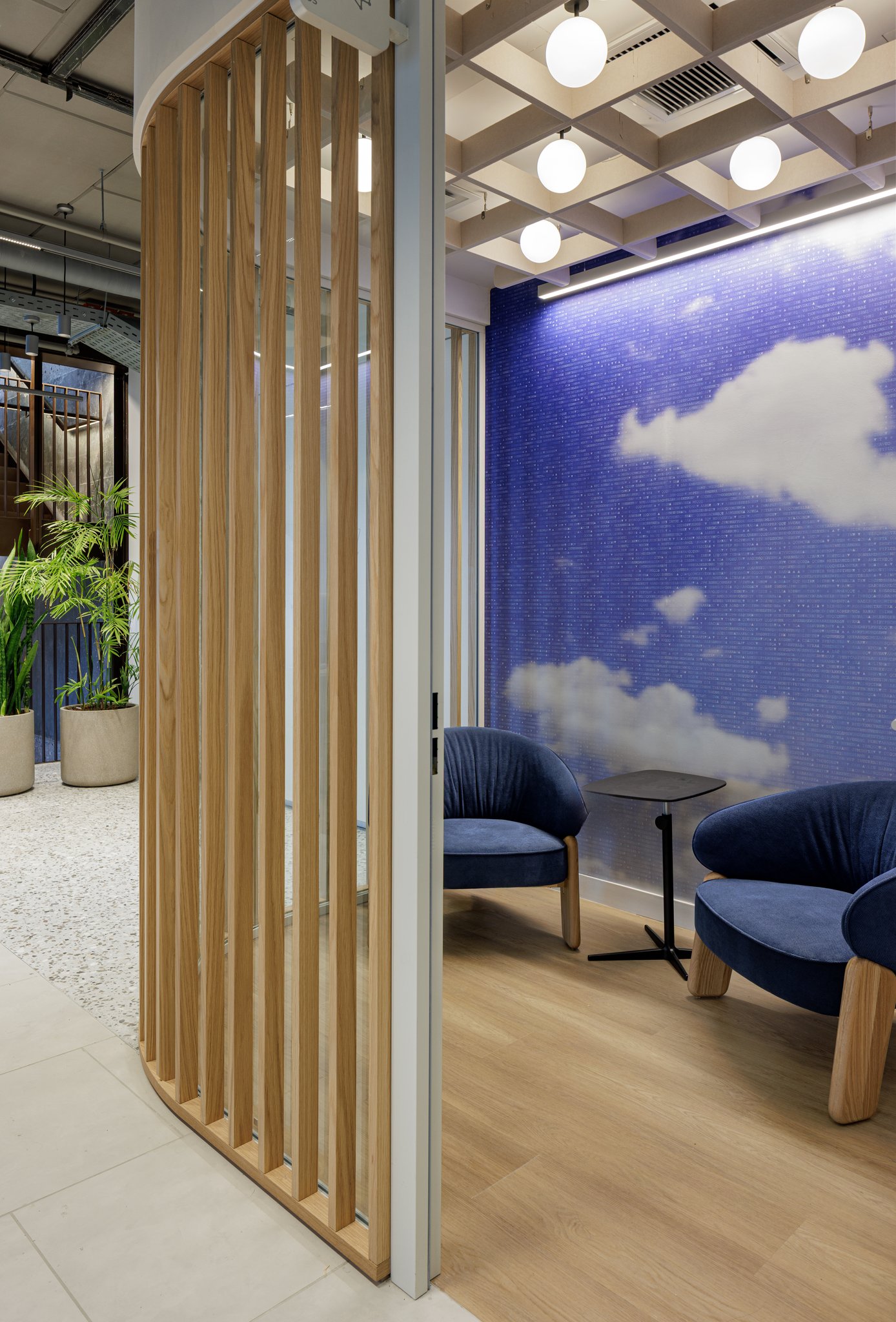 A mosaic sky wall behind a curved oak-slat partition in the lounge.
