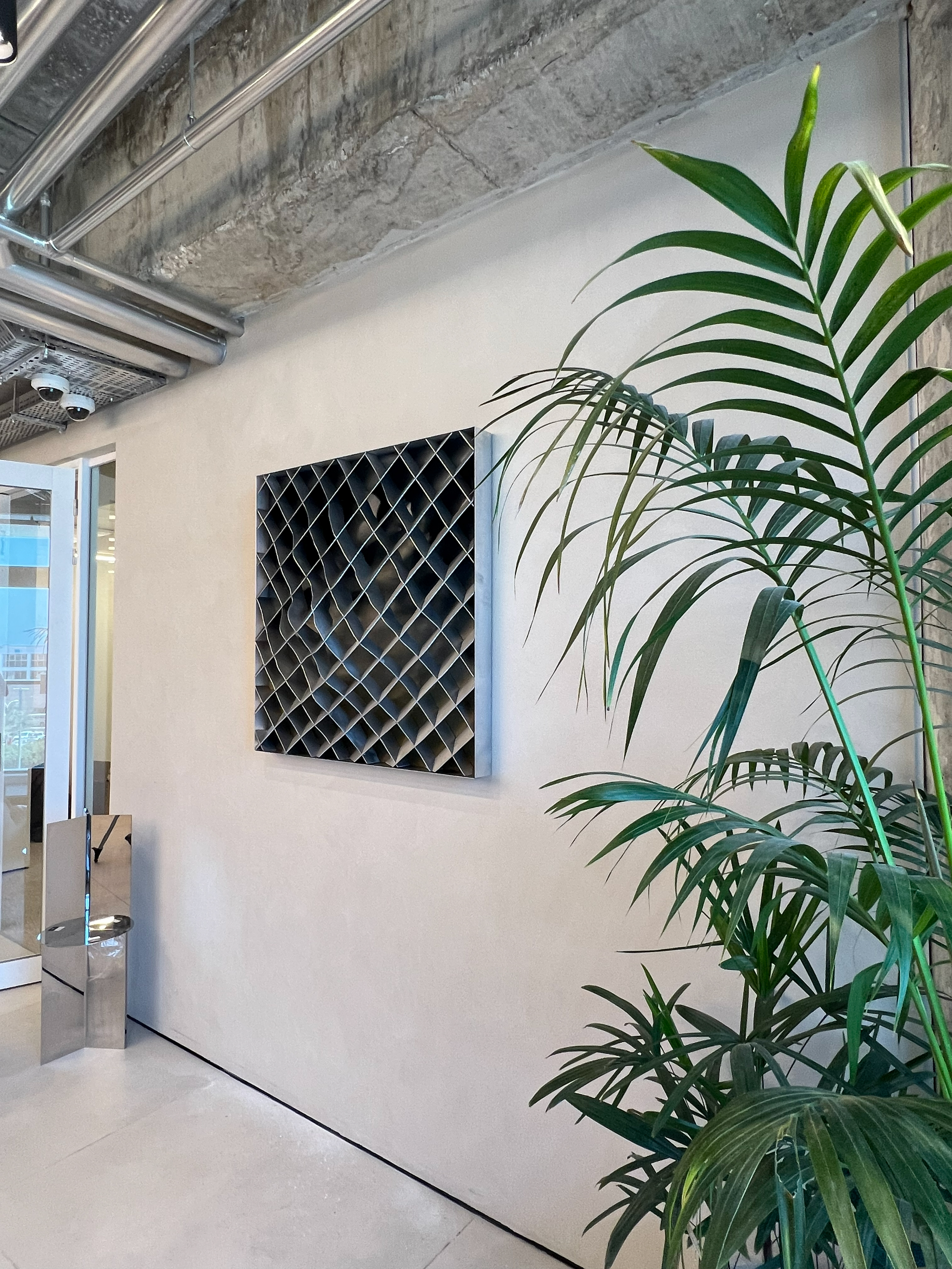 A dark diamond-mesh relief panel on the wall, topographic contours made sculptural.