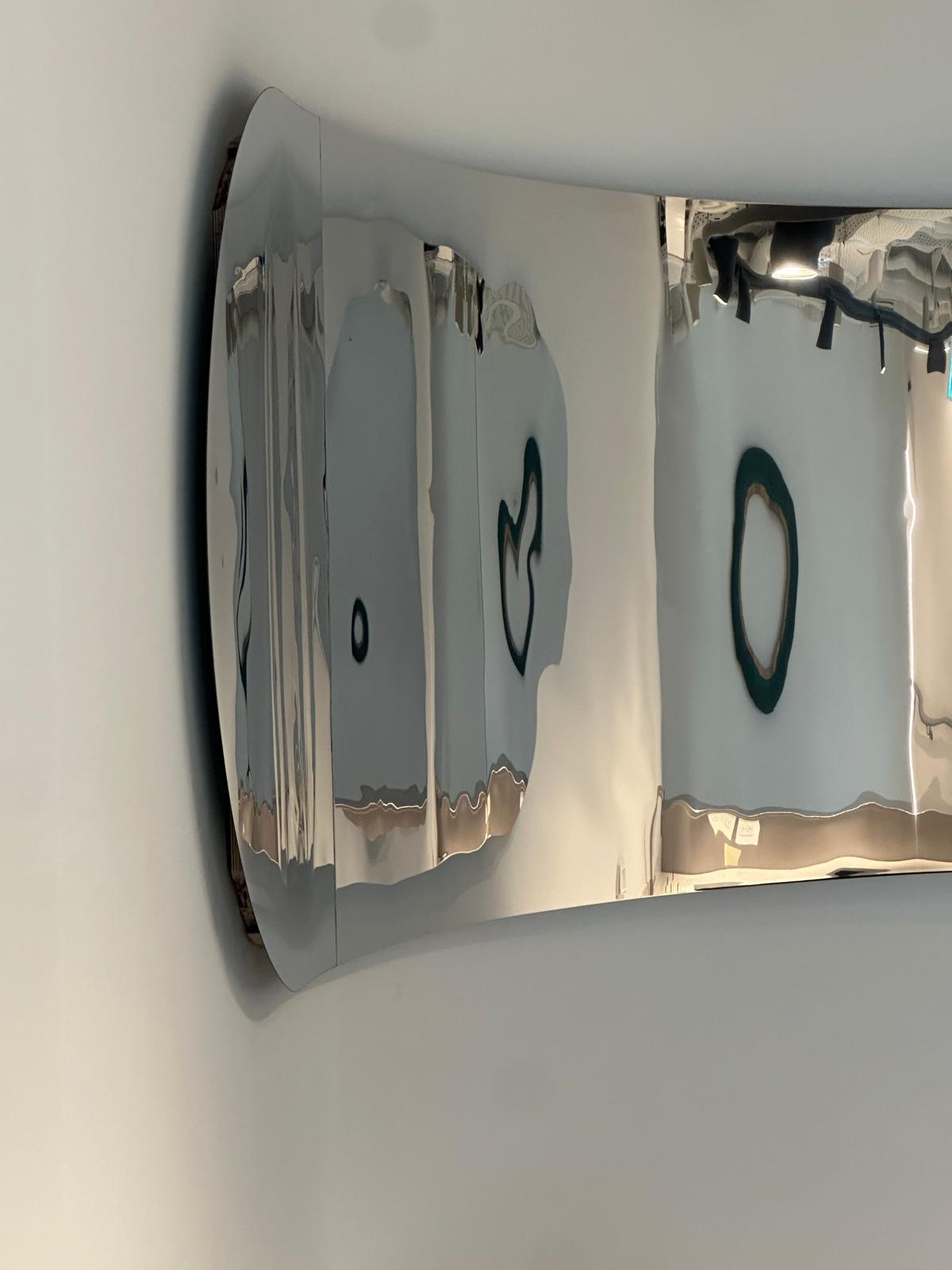 A waved sheet of mirror-polished stainless steel liquefying the wall behind it.