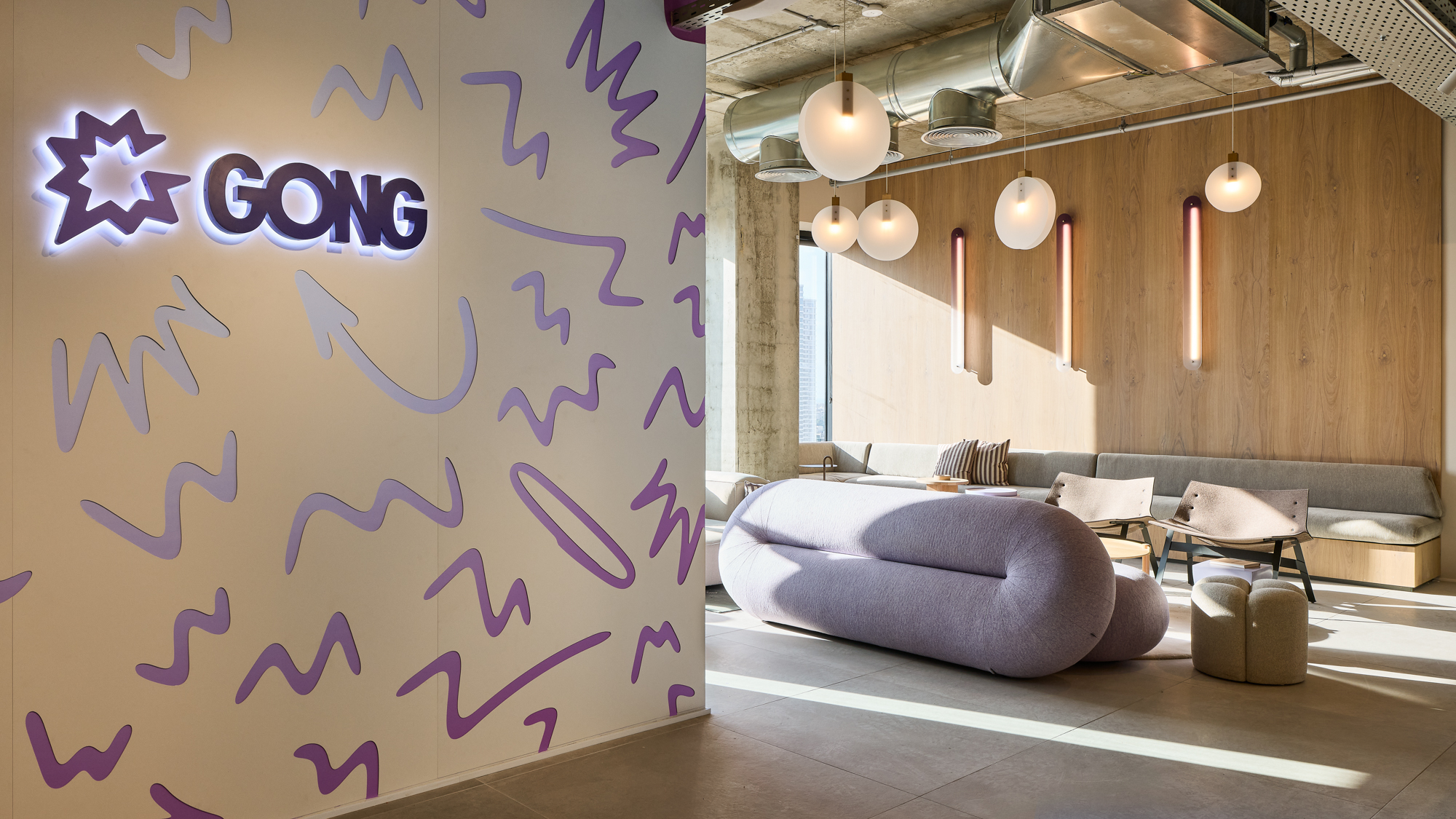 Gong's lounge — the backlit logo at the centre of a wall of hand-drawn purple marks, a lilac sofa alongside.