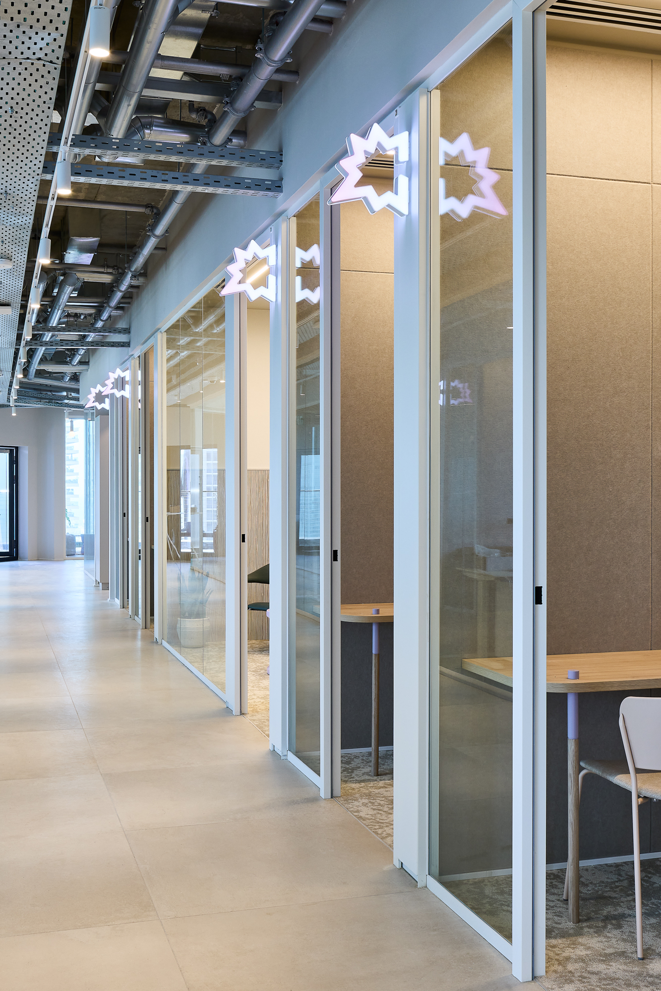 Neon Gong stars glowing above the glass meeting pods along the corridor.