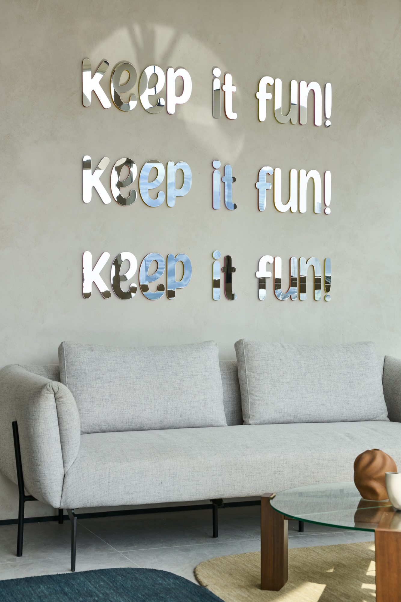 “Keep it fun!” spelled three times in mirrored acrylic letters above the lounge sofa.
