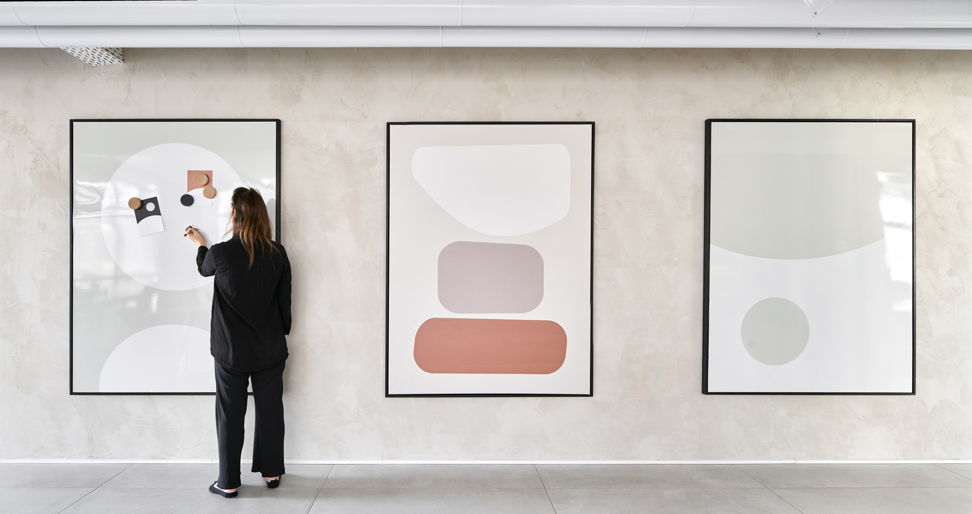 Someone writing on the left panel of a three-part writable art triptych in soft muted shapes.