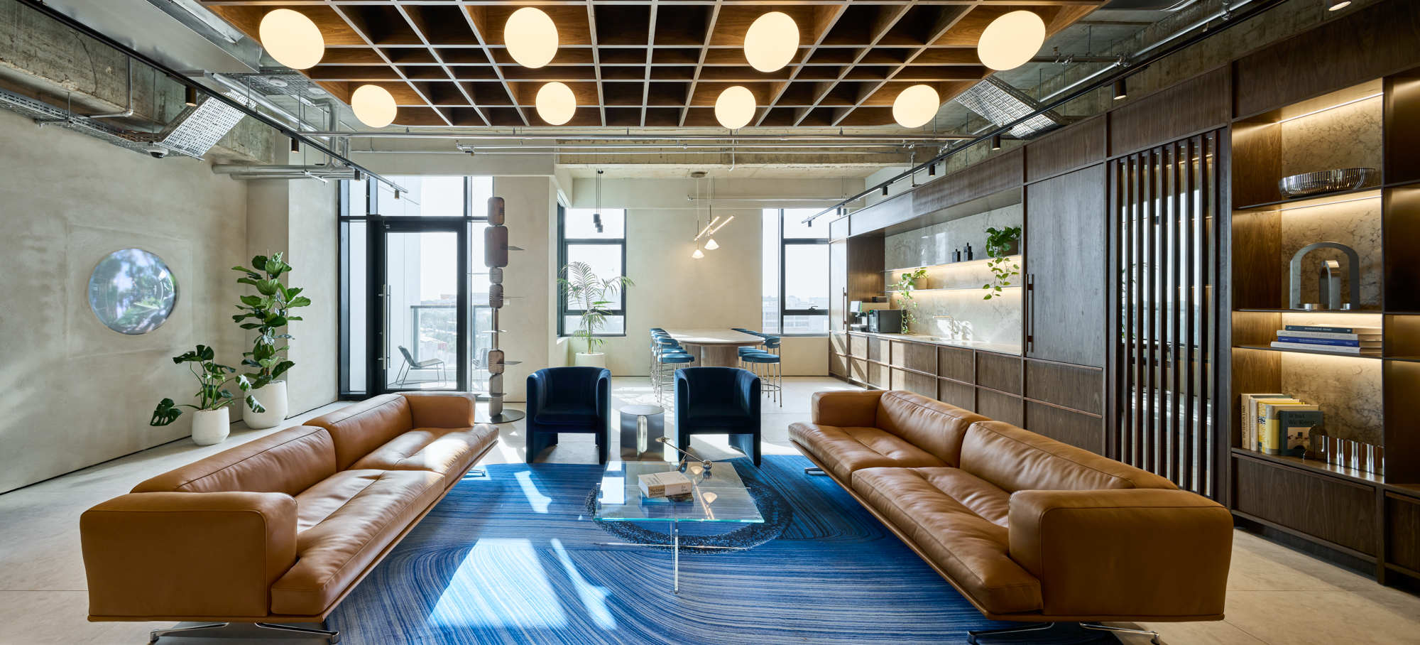 A round lens set into the concrete lounge wall, tan leather sofas and a blue rug below.
